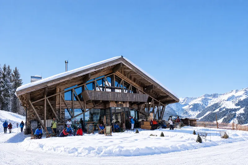 Holz-Restaurant in Berglandschaft mit Gästen auf der Terrasse