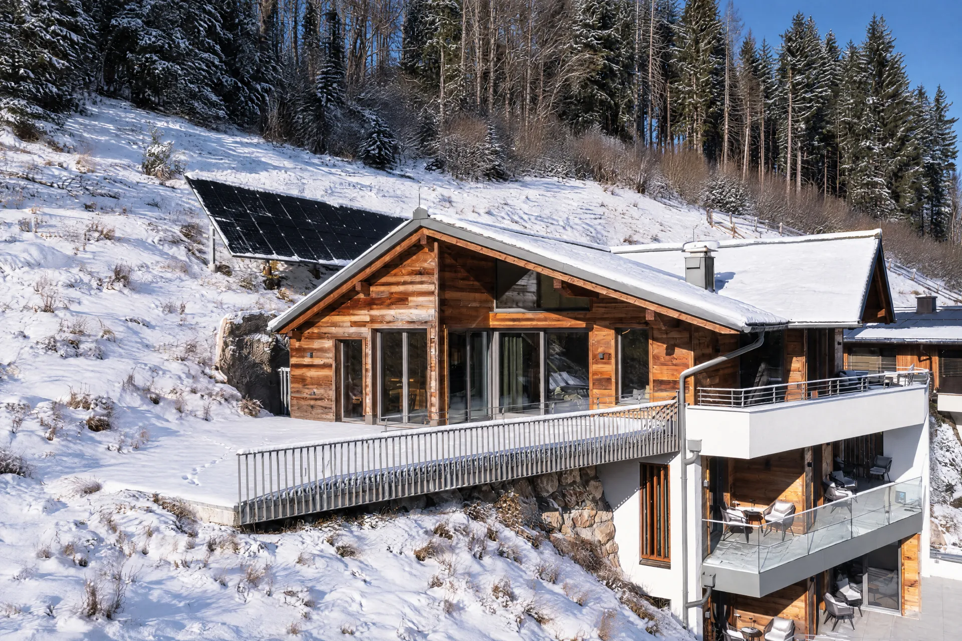 Le chalet en bois à flanc de colline avec terrasse devant des prairies enneigées