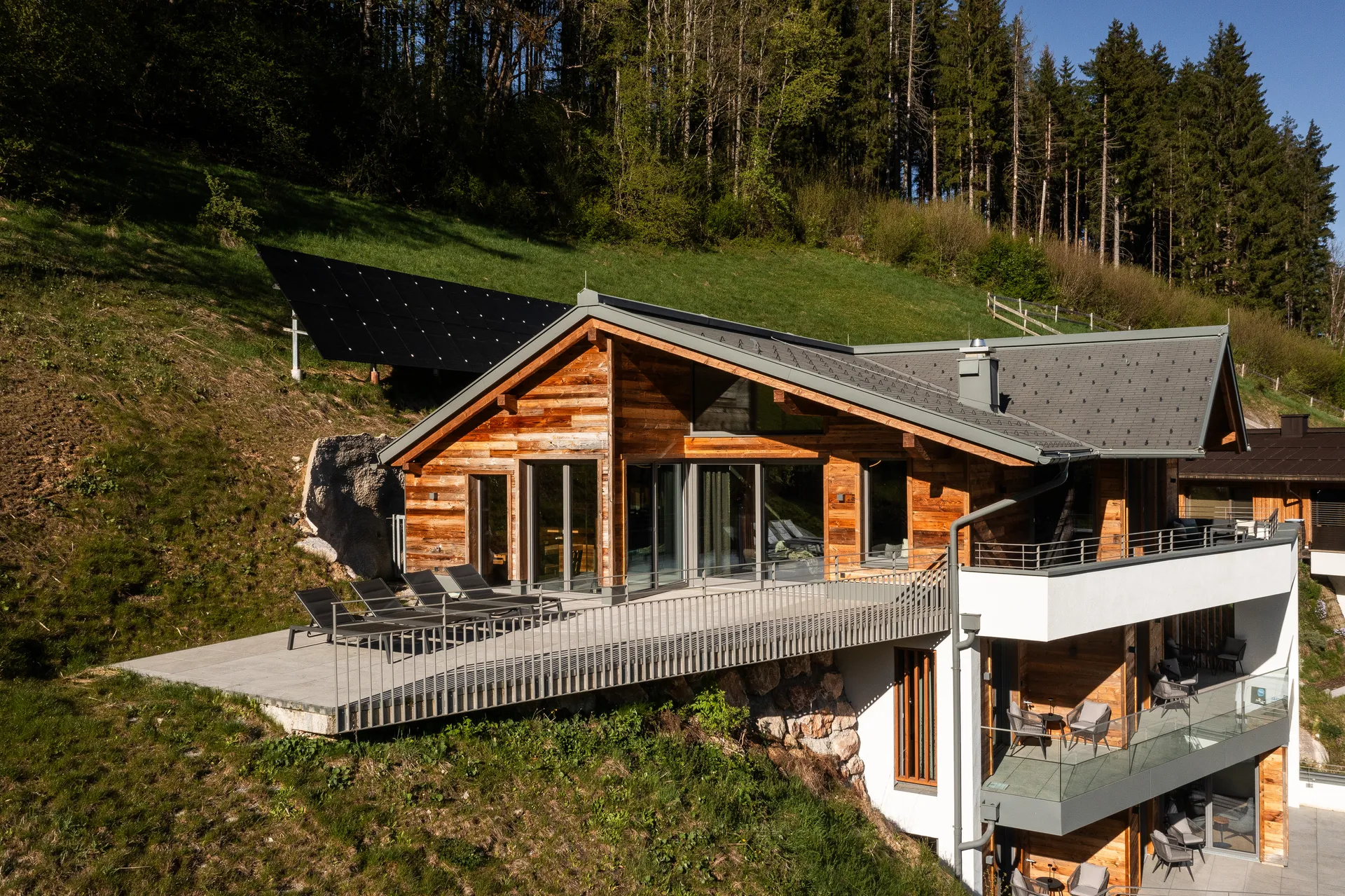 Das Holzchalet am Hang mit Terrasse und Sonnenliegen vor grünen Wiesen