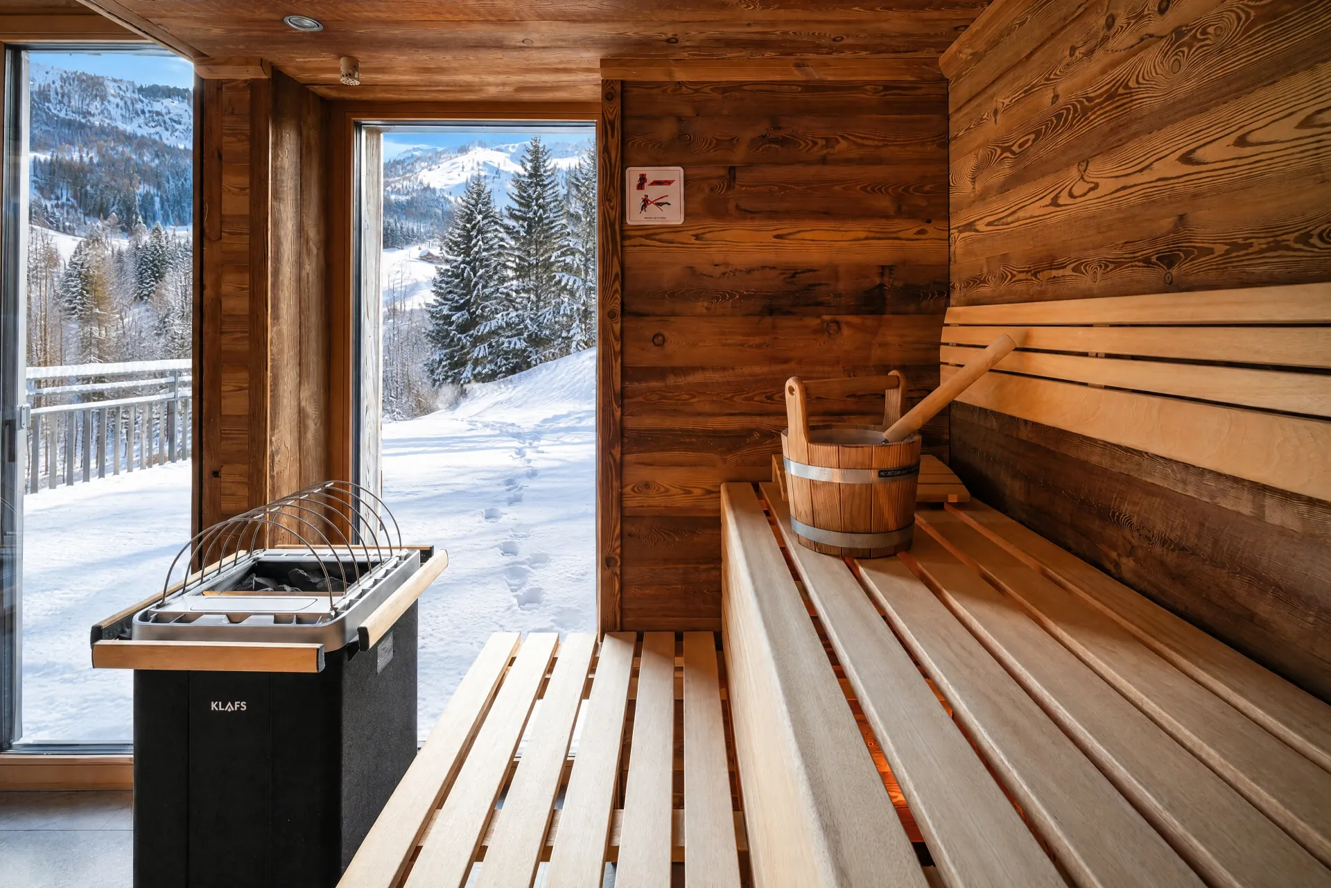 Blick aus der Klafs-Panorama-Sauna durch die Glaswand auf die verschneite Terrasse und die Berge