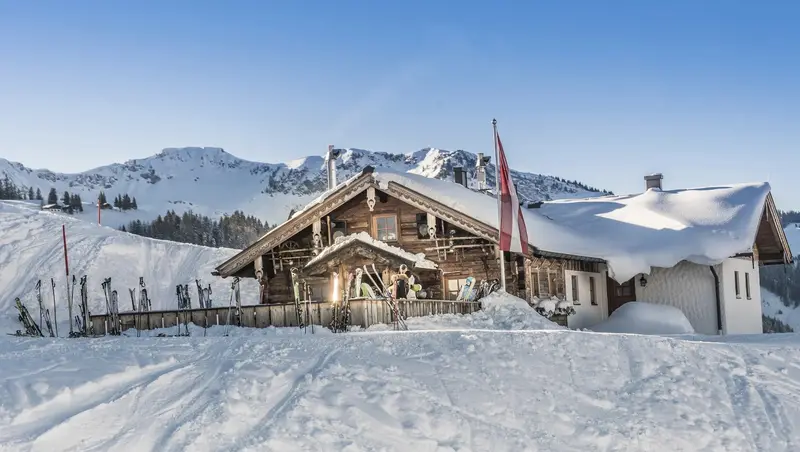Schneebedeckte Berghütte mit Skispuren und Bergen im Hintergrund
